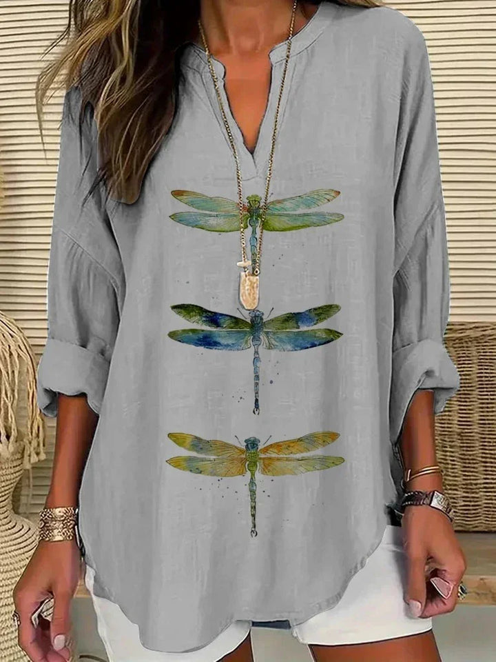 Woman wearing light gray long sleeve top with colorful dragonfly prints, white shorts, and layered necklace