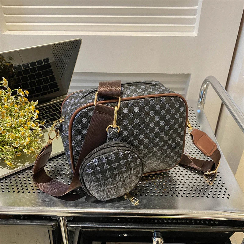 Gray patterned crossbody bag with round coin pouch and brown strap on metal surface near laptop and flowers