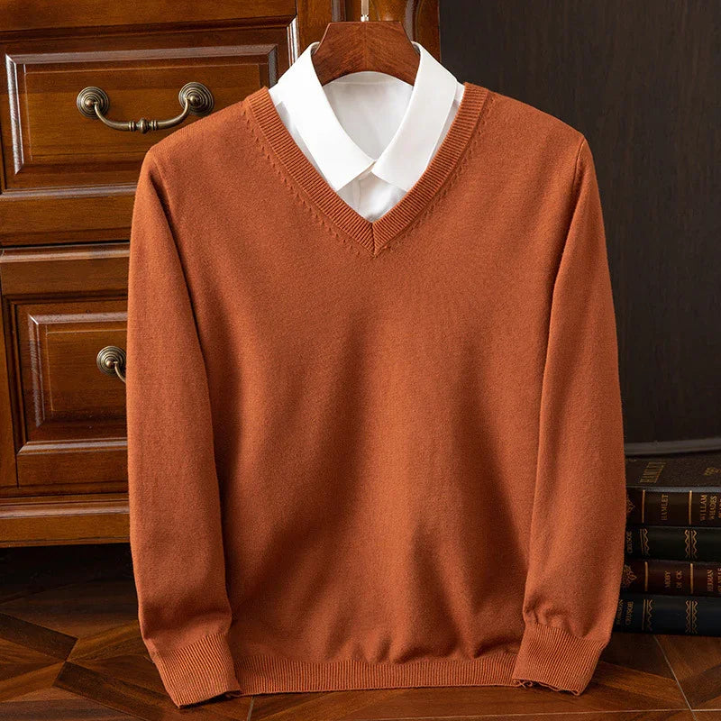 Rust orange V-neck sweater with white collared shirt on wooden hanger, classic interior background