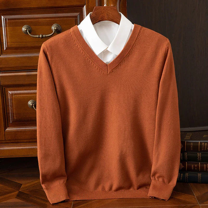 Rust orange V-neck sweater with white collared shirt on wooden hanger, classic interior background