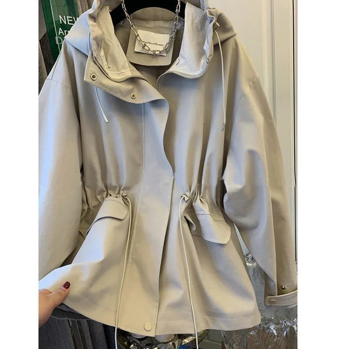 Beige hooded jacket with drawstring waist and front flap pockets hanging indoors