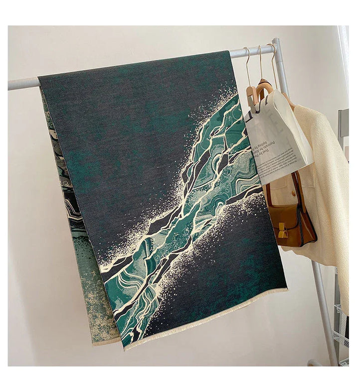 Dark green and black patterned scarf with abstract white and teal design hanging on silver rack