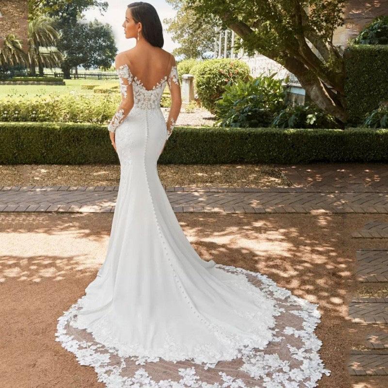 Bride in a white off-shoulder lace wedding dress with long train standing outdoors in a garden