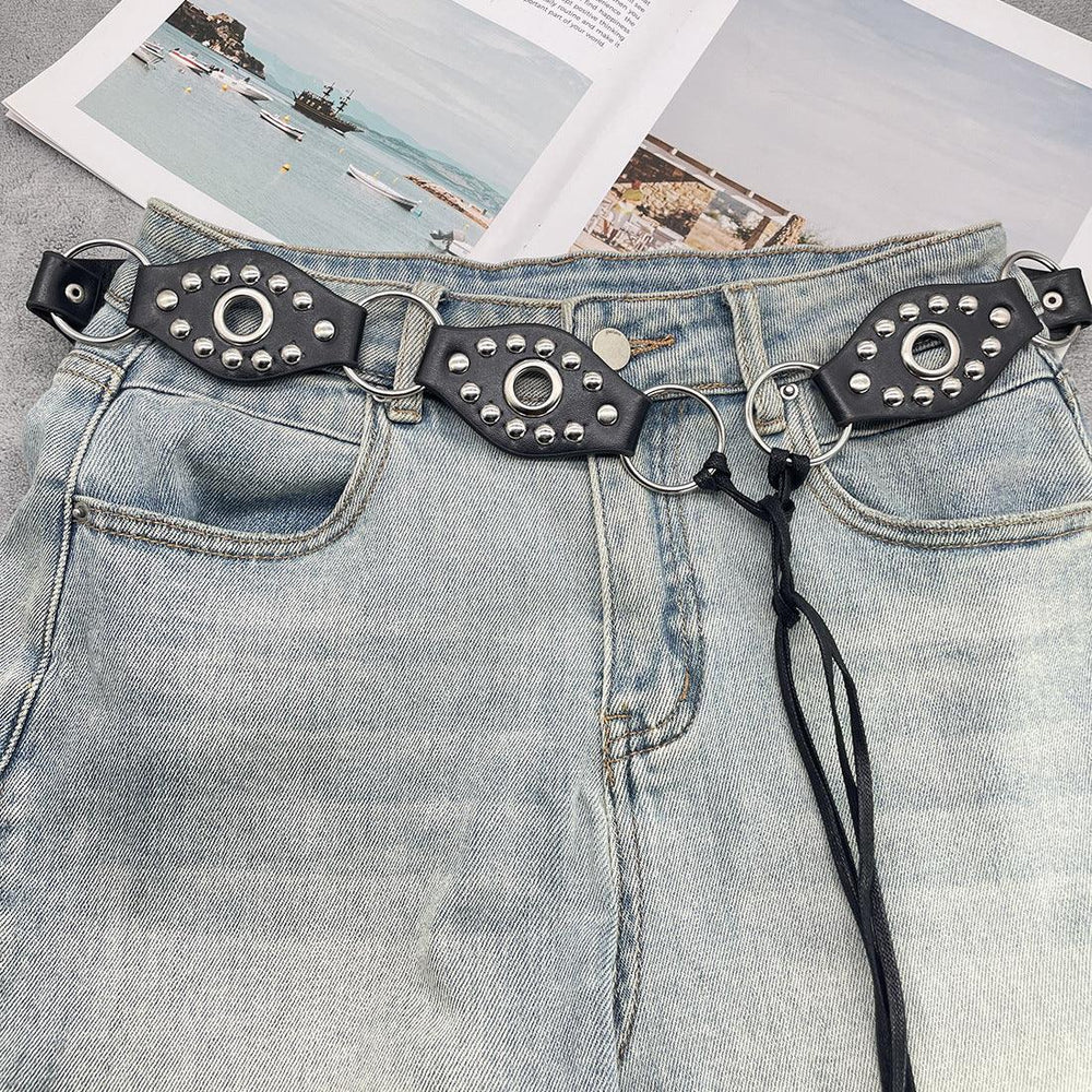 Light blue denim jeans with black studded leather belt and silver rings on a flat surface