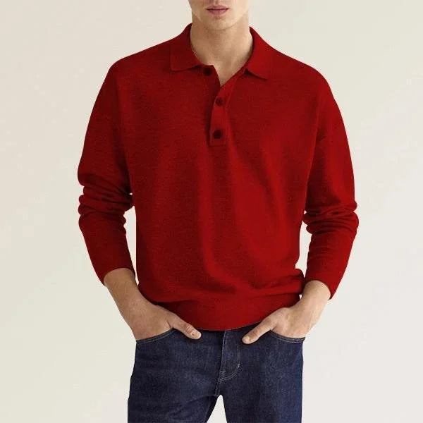 Man wearing a red long-sleeve polo shirt paired with dark blue jeans against a plain background