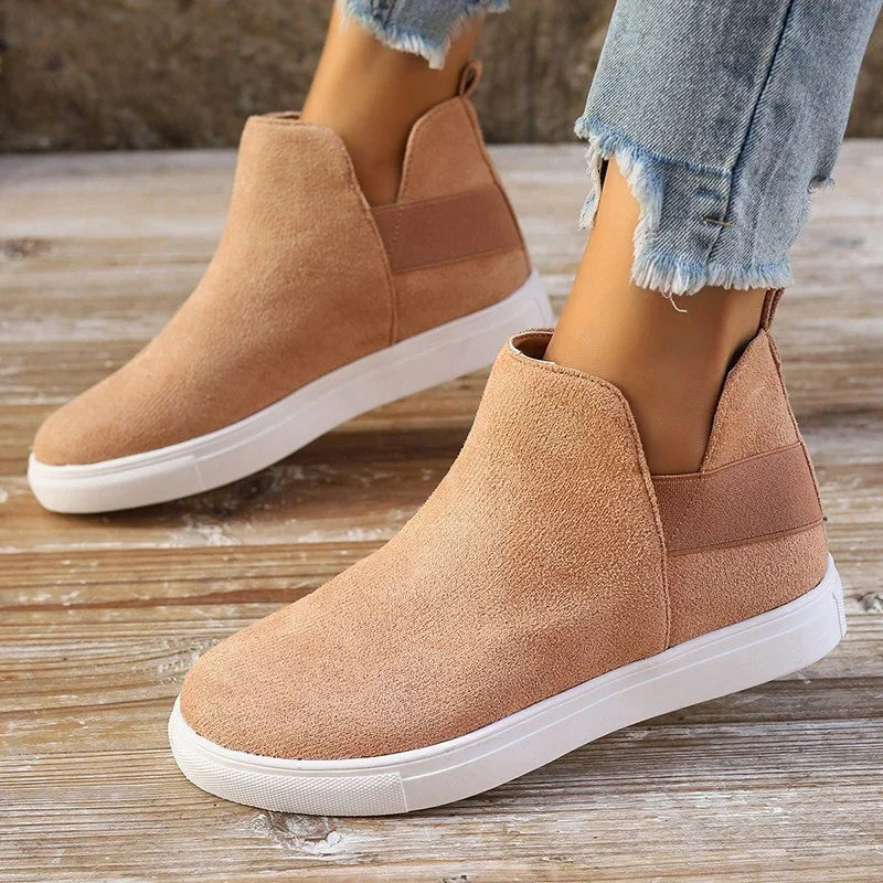 Tan suede slip-on sneakers with white rubber soles worn with frayed hem light blue jeans on wooden floor