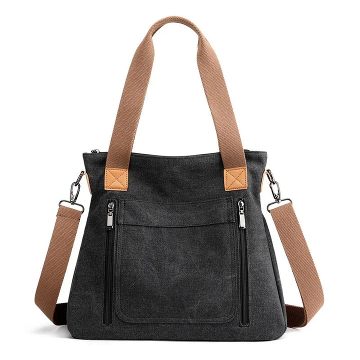 Black canvas tote bag with tan handles and removable shoulder strap, front zippered pockets