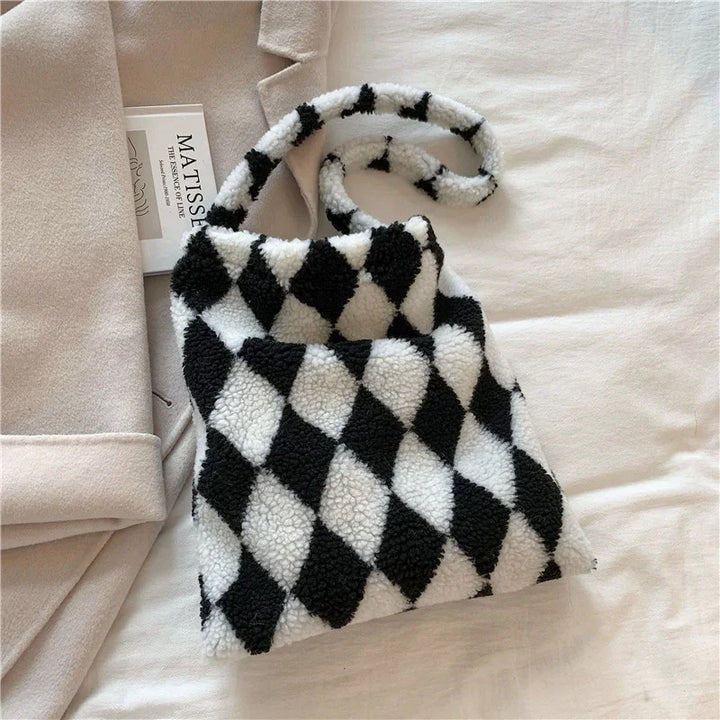 Black and white diamond pattern sherpa fleece shoulder bag on beige fabric with a book and blanket