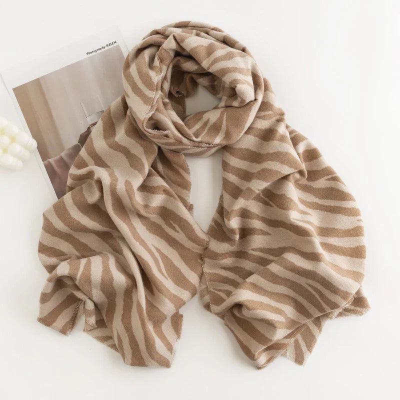 beige and light brown zebra striped cozy scarf laid on white surface with minimalistic magazine