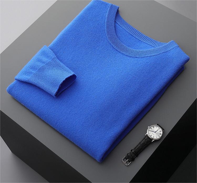 Folded bright blue wool sweater with ribbed cuffs on matte dark gray surface beside black leather strap wristwatch