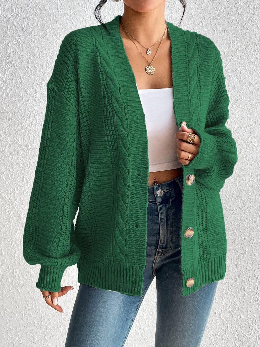 Woman wearing green cable knit cardigan with large buttons over white crop top and blue jeans