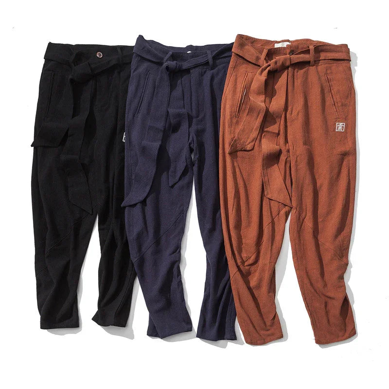 Three pairs of tapered pants in black, navy blue, and rust colors with waist ties and pockets