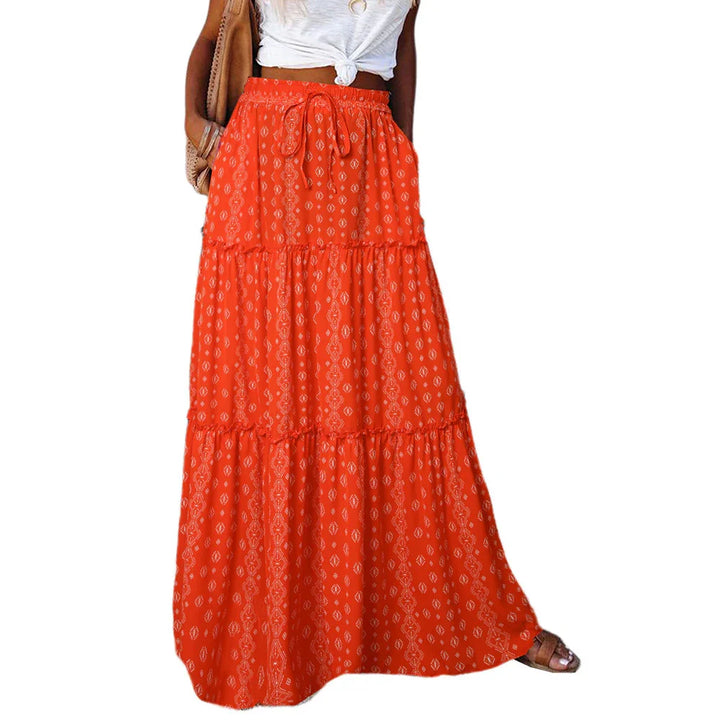 Woman wearing a bright orange patterned tiered maxi skirt with a drawstring waist and white knotted top