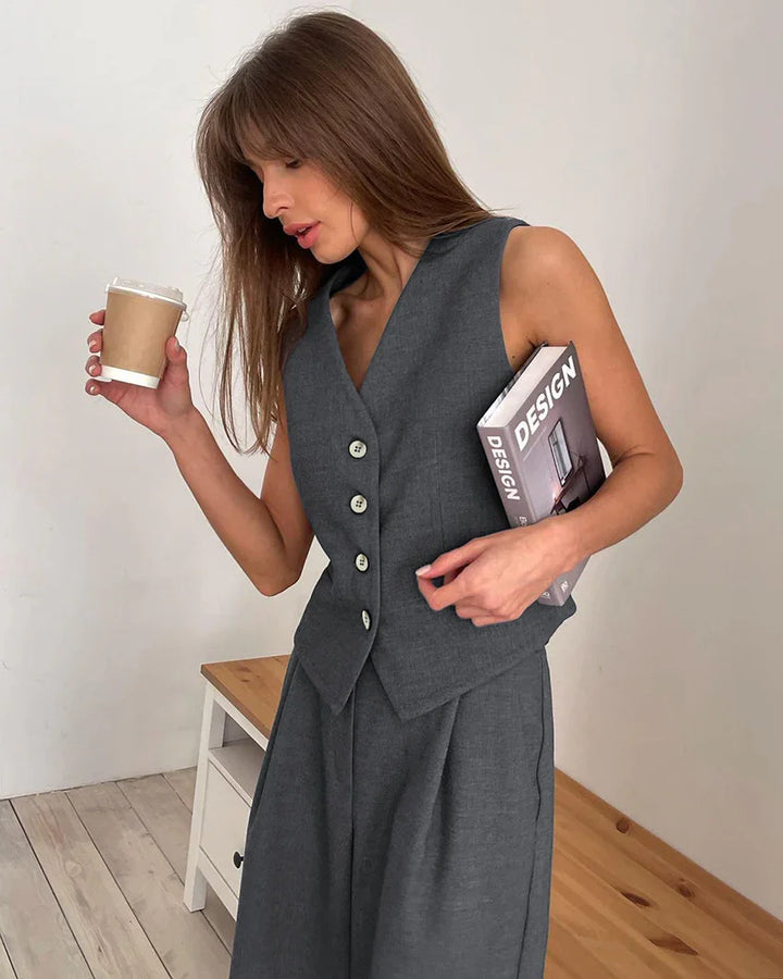 Woman in sleeveless gray vest and pants holding coffee cup and design book in minimalist room