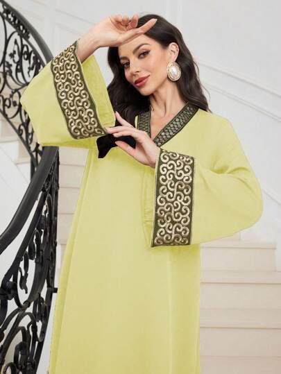 Woman posing on staircase wearing light green tunic with wide sleeves and intricate black and beige embroidery
