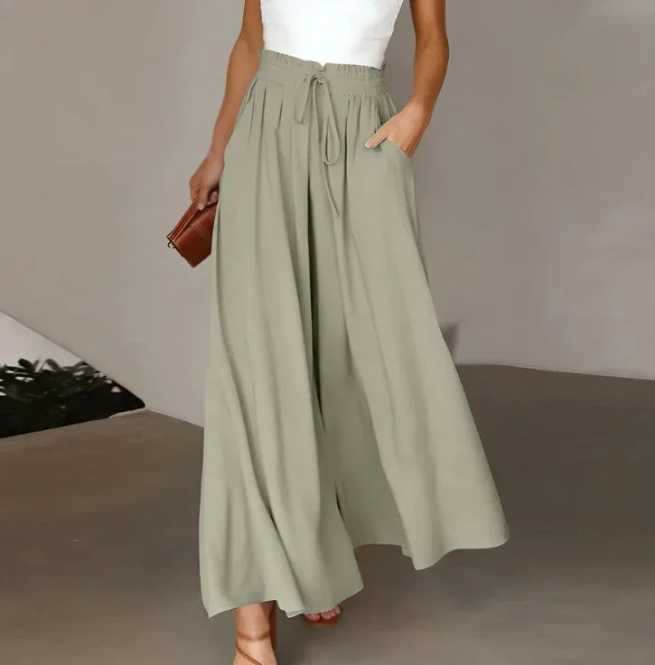 Woman wearing beige wide-leg pants with drawstring waist and pockets, holding a brown clutch