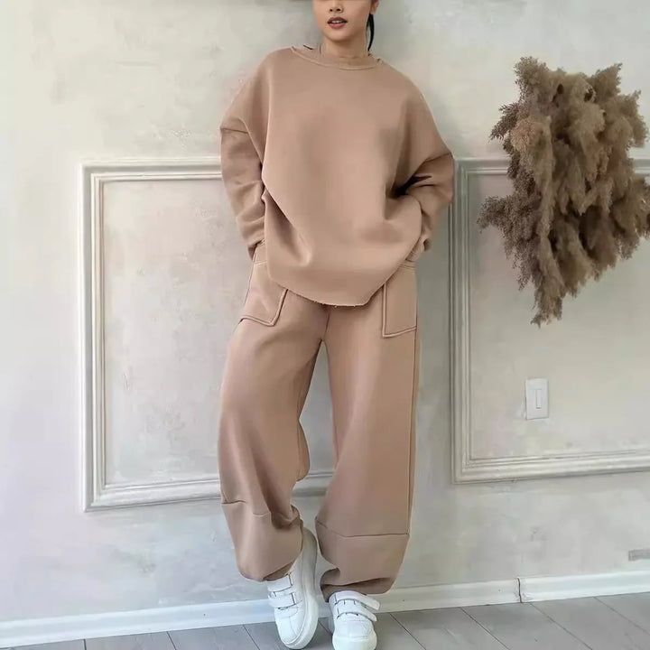 Woman wearing beige oversized sweatshirt and matching wide-leg pants with white sneakers indoors