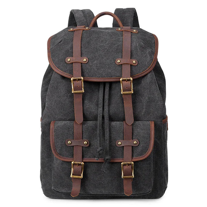Black canvas backpack with brown leather straps and brass buckles, front pocket, and top handle