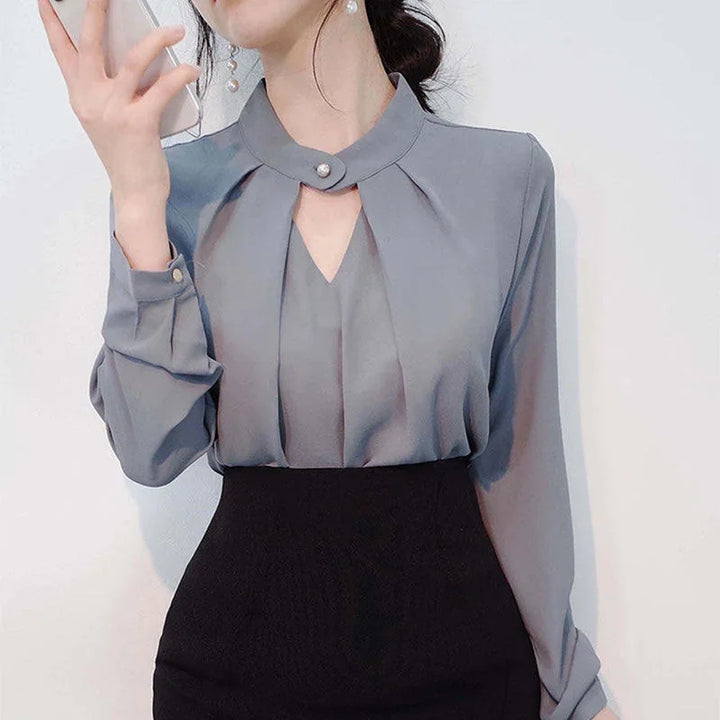 Woman wearing grey pleated blouse with pearl button collar and black high-waisted skirt