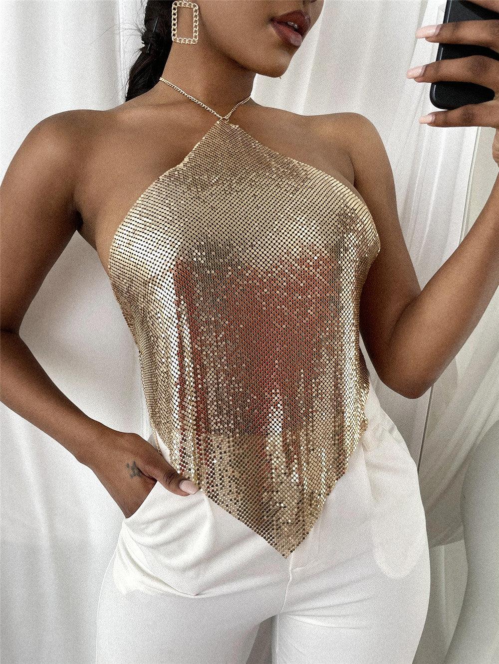 Woman wearing gold sequin halter top and white pants taking a mirror selfie