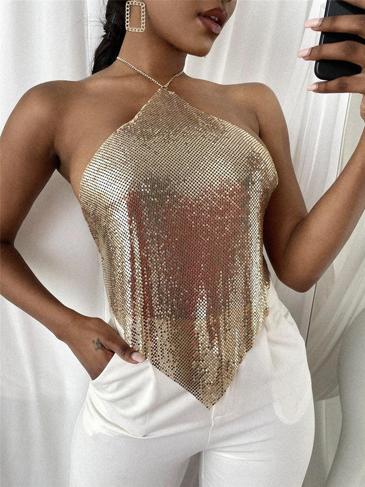 Woman wearing gold sequin halter top and white pants taking a mirror selfie