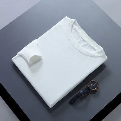 Folded white crew neck sweater with a black leather strap wristwatch on a gray surface