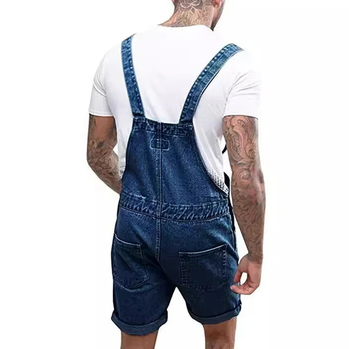 Man wearing blue denim overall shorts and white t-shirt viewed from back with tattooed arms