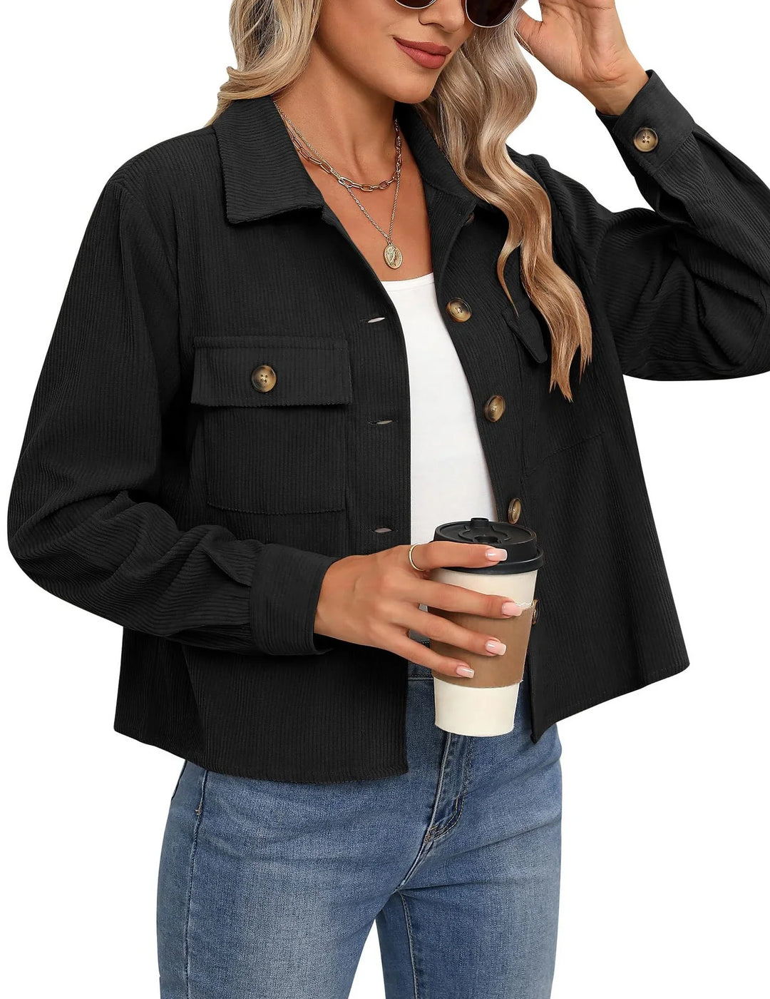 Woman wearing black button-up corduroy jacket with pockets, white top, blue jeans, holding coffee cup