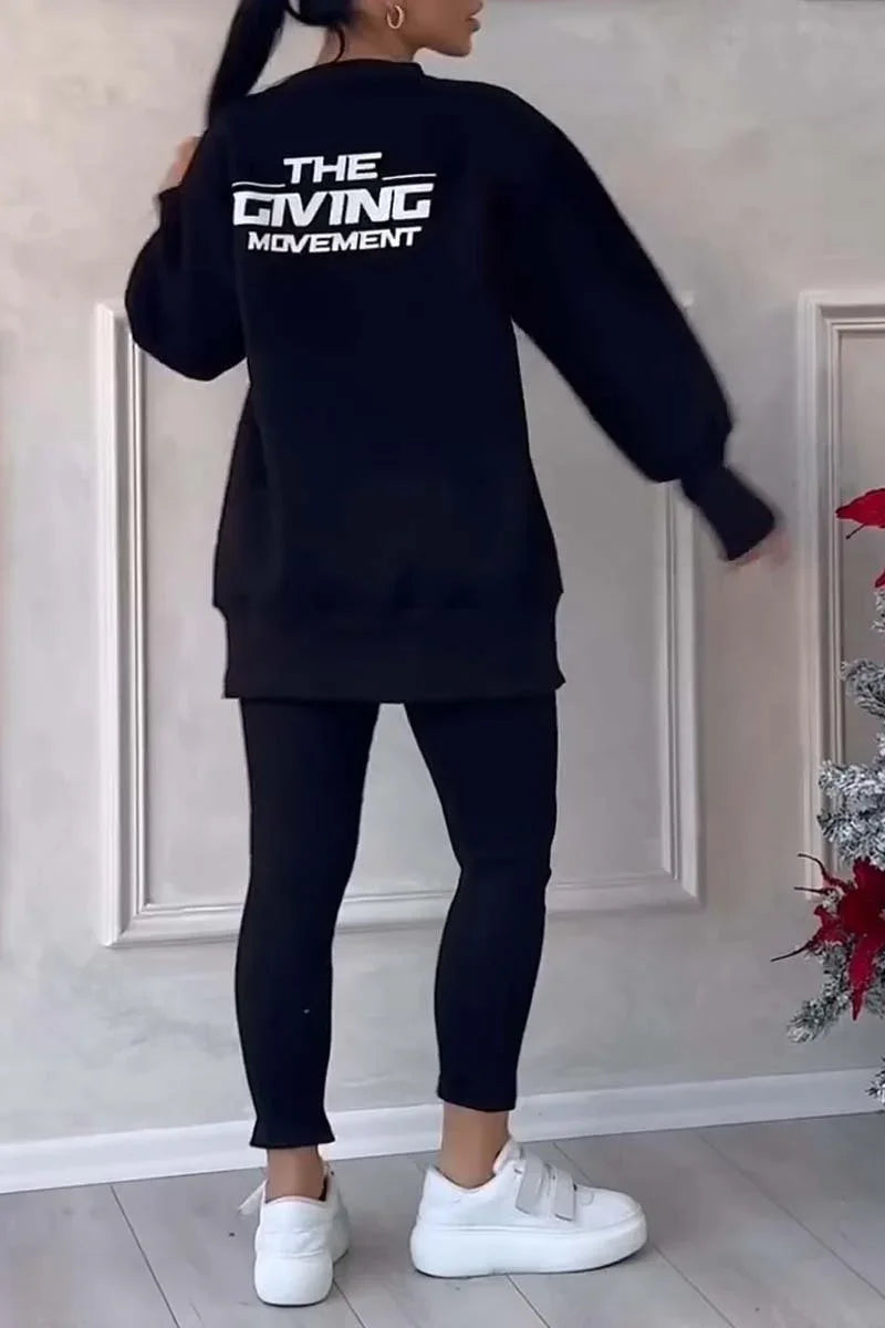 Woman wearing black oversized sweatshirt with The Giving Movement logo, black leggings, white sneakers