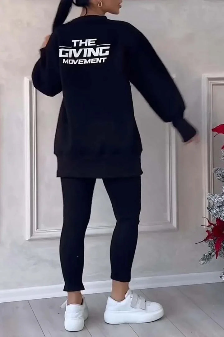 Woman wearing black oversized sweatshirt with The Giving Movement logo, black leggings, white sneakers
