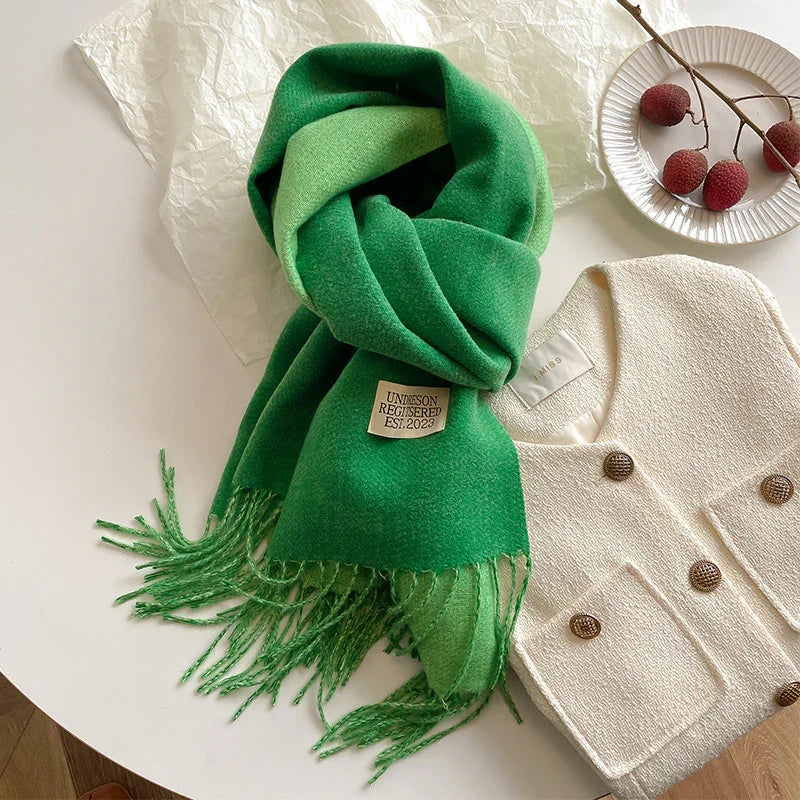 Green wool scarf with fringes and label, paired with white textured double-breasted jacket on table