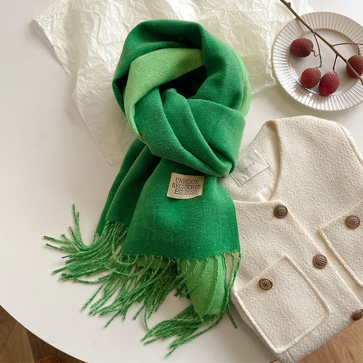 Green wool scarf with fringes and label, paired with white textured double-breasted jacket on table