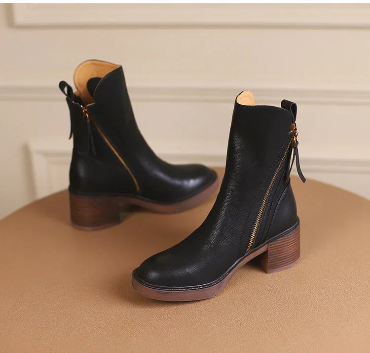 black leather ankle boots with side zippers and wooden block heels on a brown surface