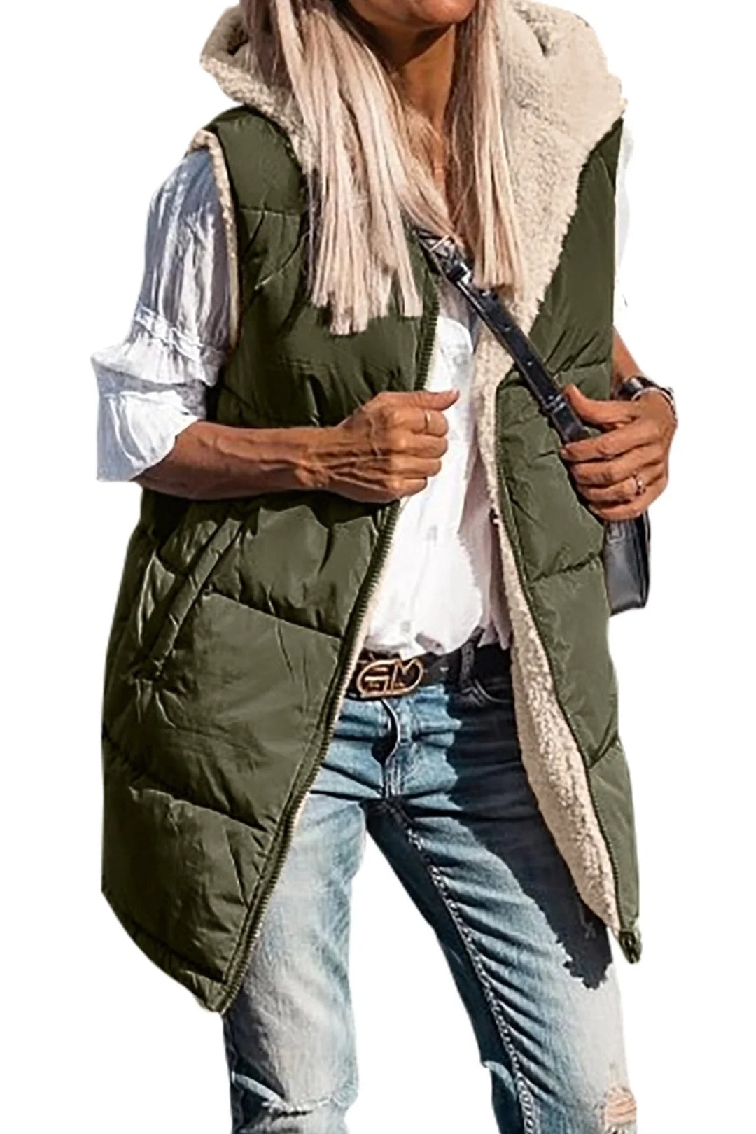 Woman wearing green quilted sleeveless hooded vest with white sherpa lining, white blouse, and blue jeans