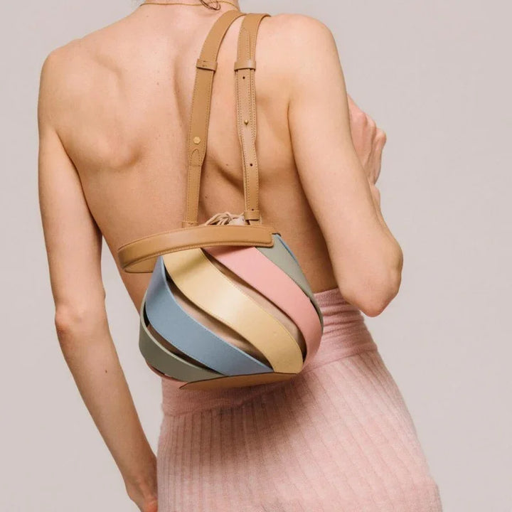 Back view of a woman wearing a colorful spiral leather backpack with tan straps and a pink skirt