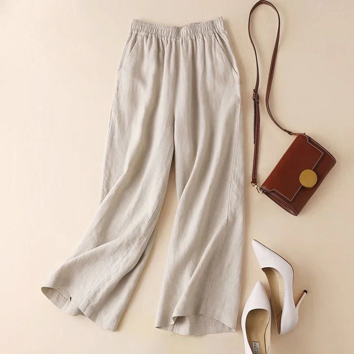 Beige wide-leg linen pants with elastic waist, brown leather crossbody bag, and white high heel shoes
