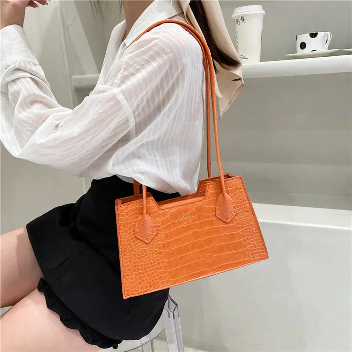 Woman wearing white blouse and black skirt holding a small orange crocodile texture handbag