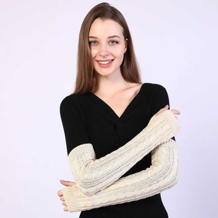 Smiling woman wearing black sweater with beige cable knit long sleeves against light background