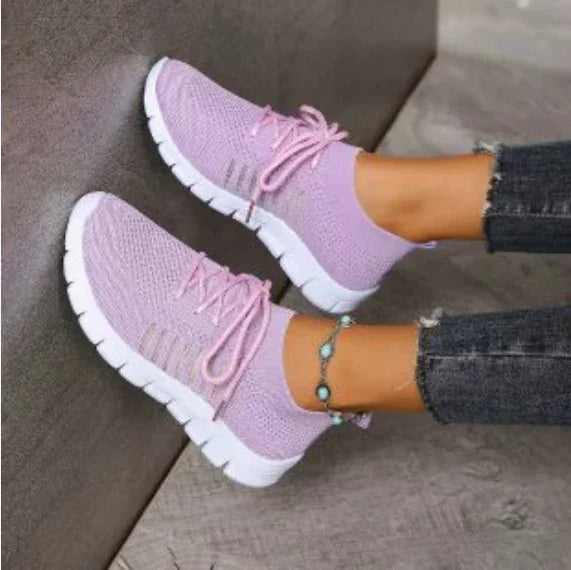 Light purple knitted athletic sneakers with white soles worn with black ripped jeans and turquoise ankle bracelet
