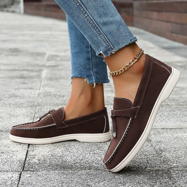 brown suede loafers with white soles worn with frayed hem blue jeans and a gold anklet on city pavement