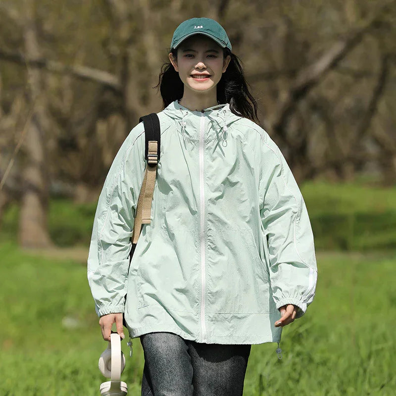 Young woman wearing light green windbreaker and green cap walking outdoors in grassy park