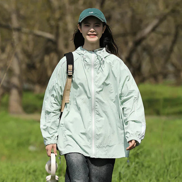 Young woman wearing light green windbreaker and green cap walking outdoors in grassy park