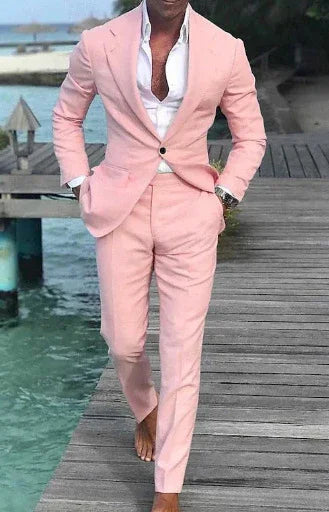 Man in stylish light pink suit and white shirt walking barefoot on wooden dock by water