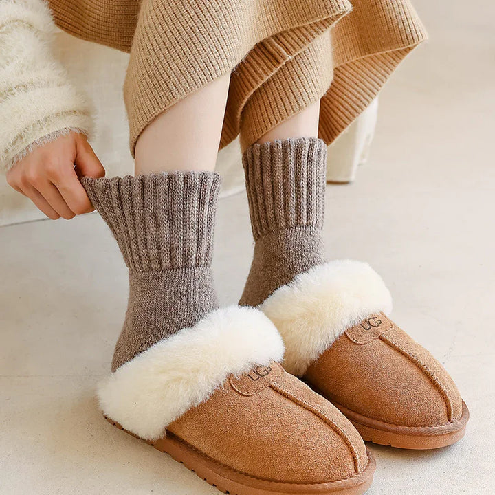 Person wearing brown UGG slippers with white fur lining and cozy gray knit socks indoors