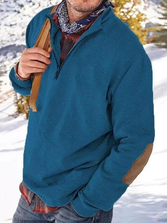 Man wearing blue quarter-zip pullover with elbow patches, plaid shirt, bandana, and backpack in snowy outdoor setting