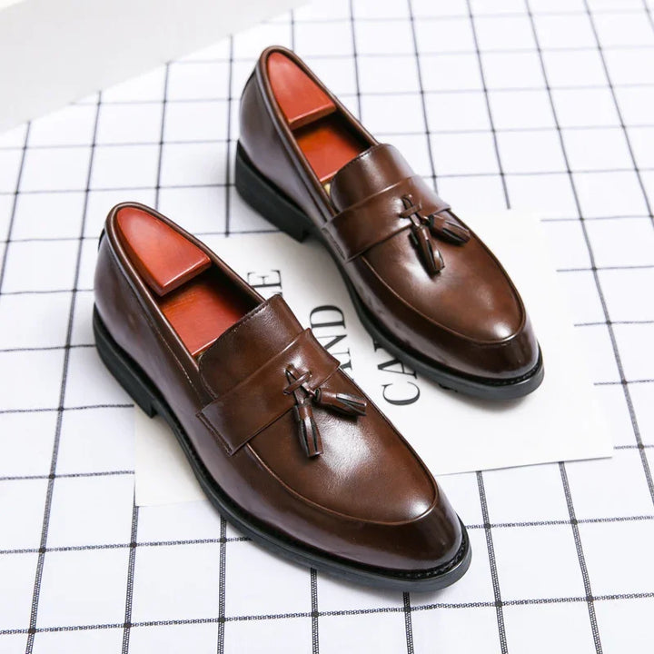 Pair of brown leather tassel loafers on white grid-patterned surface for men's formal wear