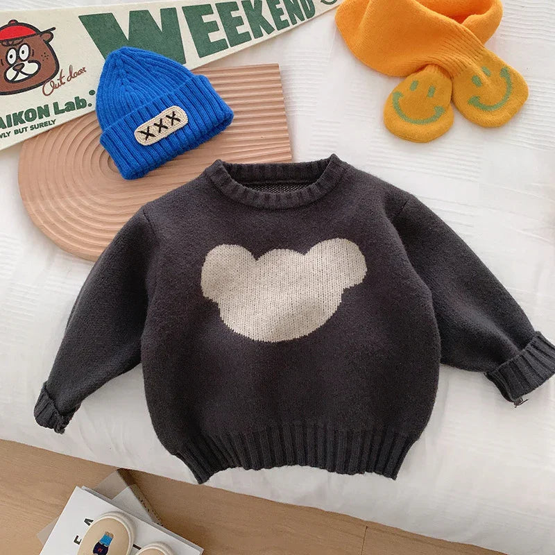 Black children's sweater with white bear silhouette, blue knit hat, and orange scarf with smiley faces