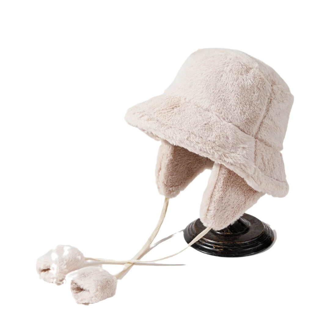 Beige faux fur bucket hat with ear flaps and pom-pom ties on black stand