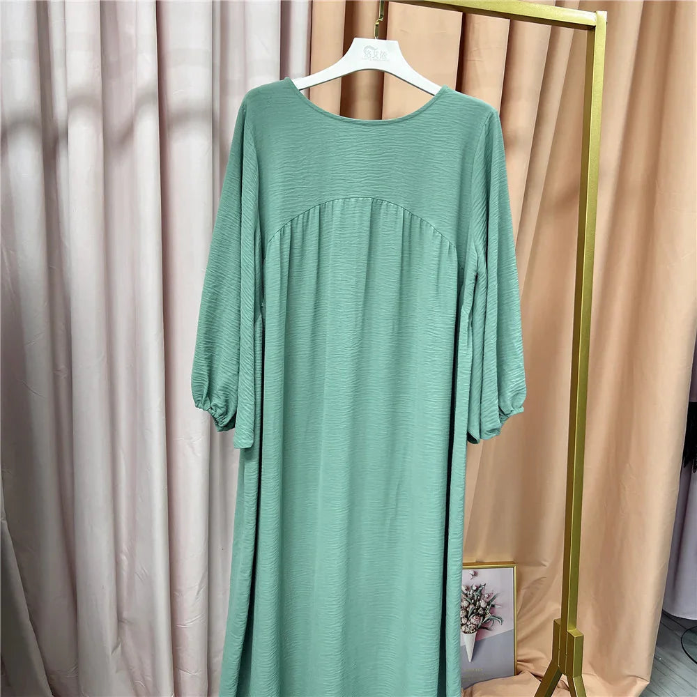 Mint green long sleeve textured dress hanging on white hanger against beige and pink curtains