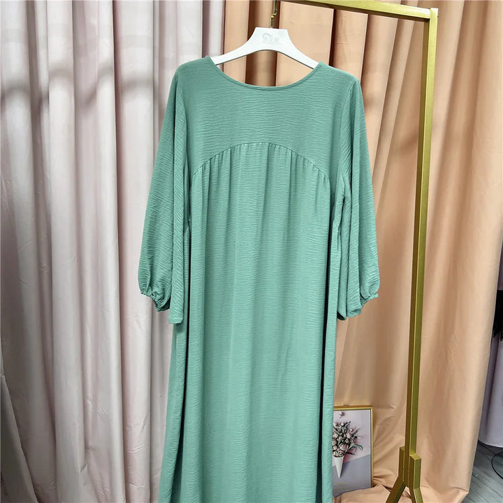 Mint green long sleeve textured dress hanging on white hanger against beige and pink curtains
